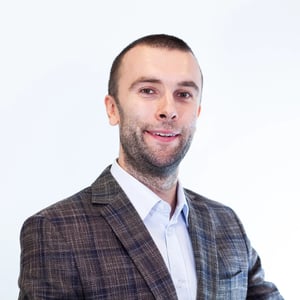 Porträt eines Mannes im karierten Sakko und weißen Hemd, der leicht lächelnd in die Kamera schaut.