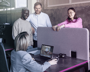 Grupo de compañeros conversando alrededor de un portátil en una oficina moderna.