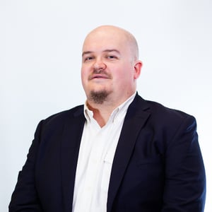 Porträt eines Mannes im dunklen Anzug und weißen Hemd, der mit leichtem Lächeln in die Kamera schaut.