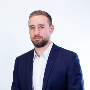 Porträt eines Mannes im dunkelblauen Anzug und weißen Hemd, der mit neutralem Ausdruck in die Kamera blickt.