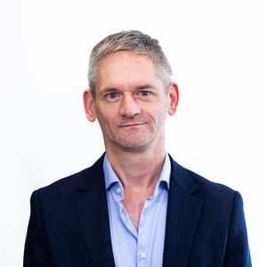 Porträt eines Mannes im dunklen Sakko und hellblauem Hemd, der mit neutralem Ausdruck in die Kamera blickt.