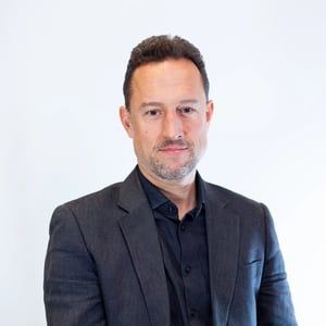 Portrait of a man in a dark suit, looking at the camera with a neutral expression.