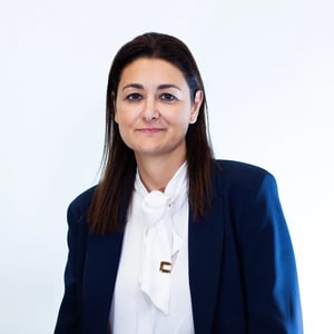 Porträt einer Frau in weißer Bluse und dunklem Blazer, die mit leichtem Lächeln in die Kamera schaut.