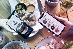 Dos personas sostienen teléfonos con aplicaciones de comida abiertas mientras cenan en una mesa de restaurante.